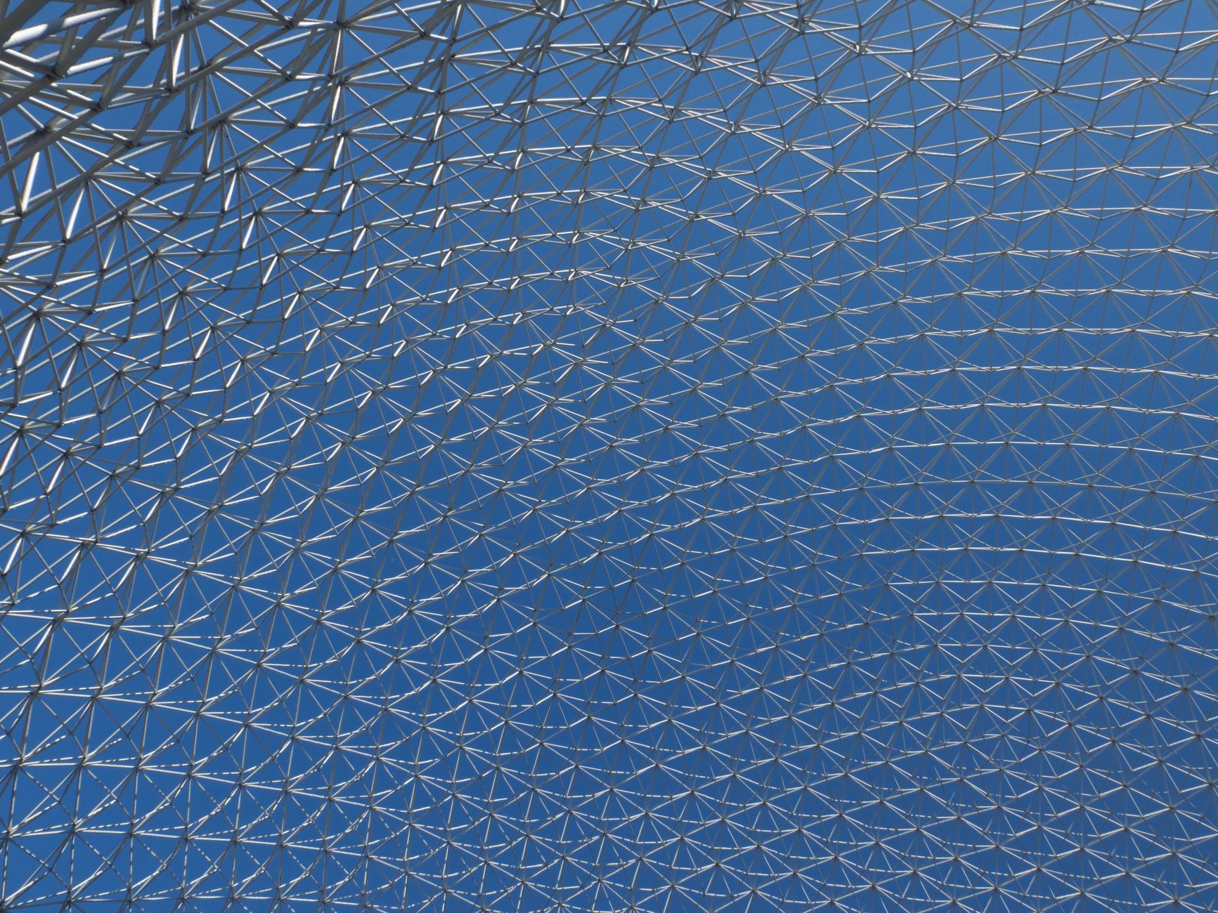 Close-up of a modern geodesic dome structure with intricate metal patterns against a clear blue sky.